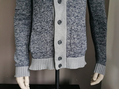 Nous façonnons le cardigan avec des boutons. Gris bleu mélangé. Taille M.